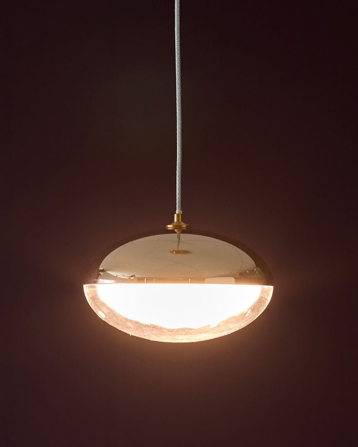 Nina single pendant light in soft gold with frosted glass bowl, suspended by white cord against dark background.