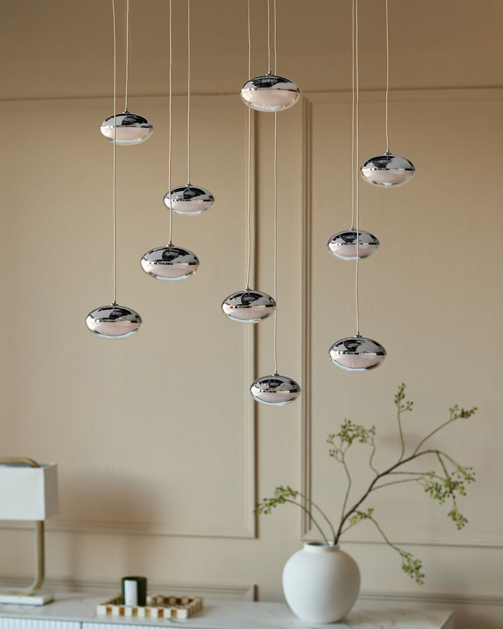 Chrome pendant lights with disc-shaped glass shades hanging at varying heights against a beige wall.