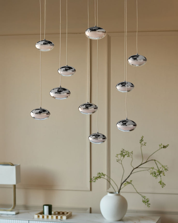 Chrome pendant lights with disc-shaped glass shades hanging at varying heights against a beige wall.