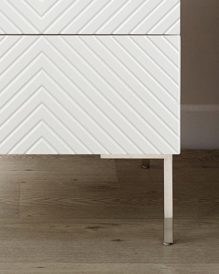 Noah white bedside table with chevron drawer fronts, metal legs, side view on wood flooring.