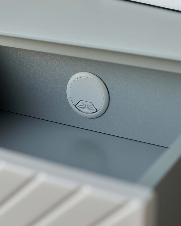 Close up of a grey desk featuring a circular cable tidy with a fan detail. Office or home working furniture.
