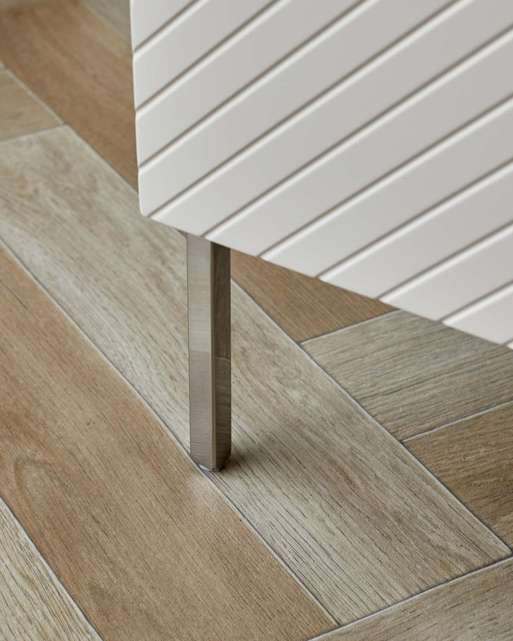 Contemporary furniture with a slatted design, standing on sleek, metal legs atop a light wood-effect herringbone floor.