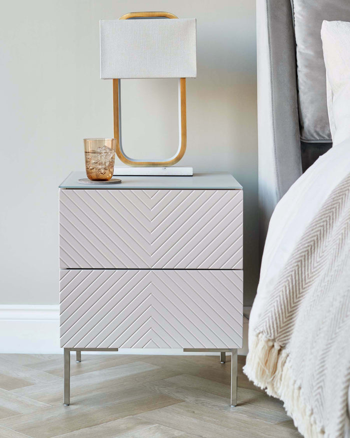 Modern bedside table with a glass top, resting on metal legs. A stylish lamp and drink sit on top.