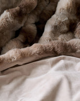 Nova throw blanket in natural color, draped and layered on neutral bedding, showing soft texture and neutral tones.