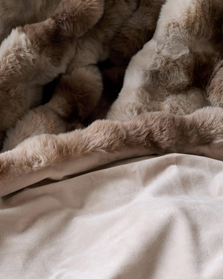 Nova throw blanket in natural color, draped and layered on neutral bedding, showing soft texture and neutral tones.