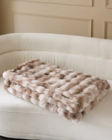 Nova throw blanket in natural, quilted pattern, draped on cream curved sofa.