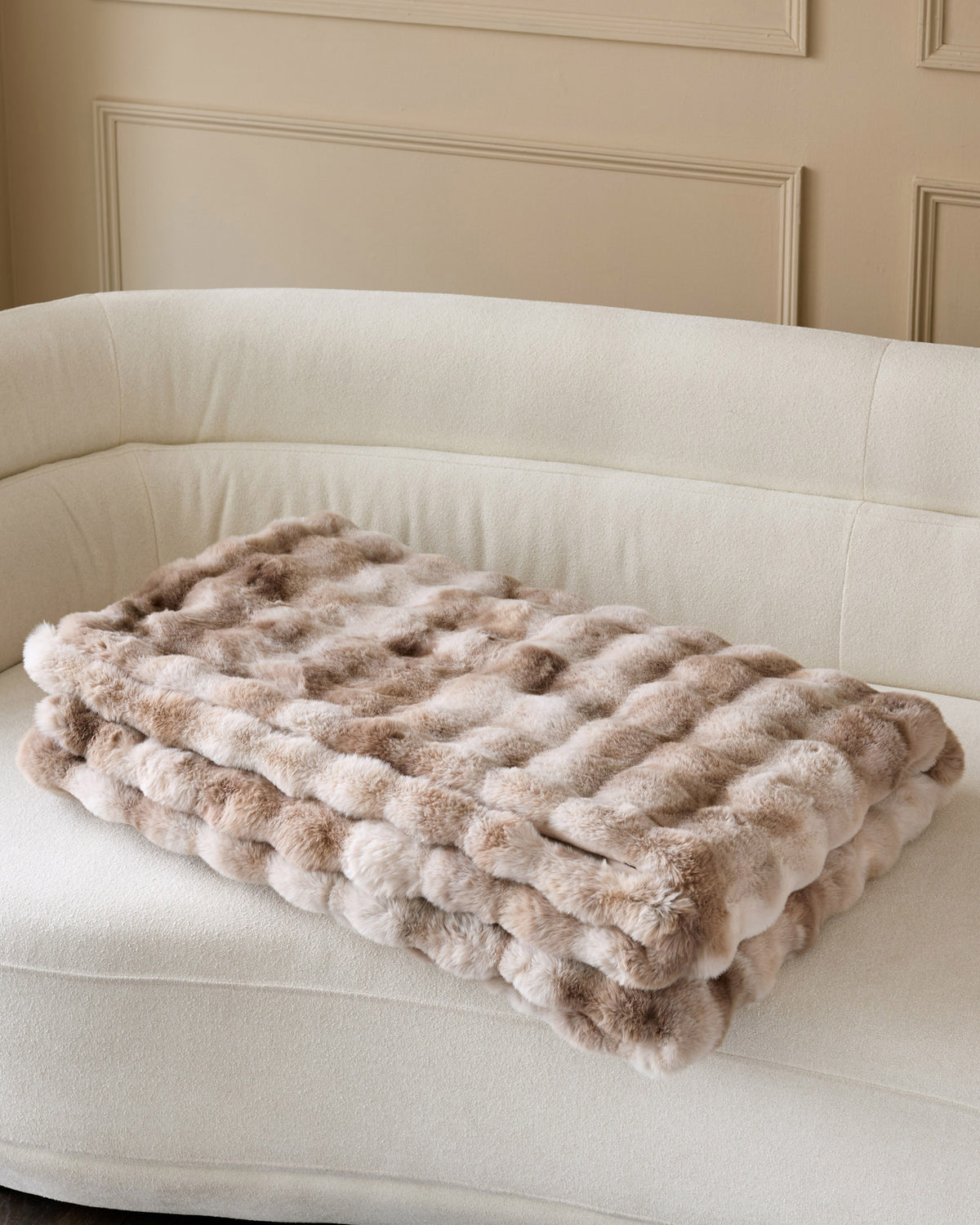 Nova throw blanket in natural, quilted pattern, draped on cream curved sofa.