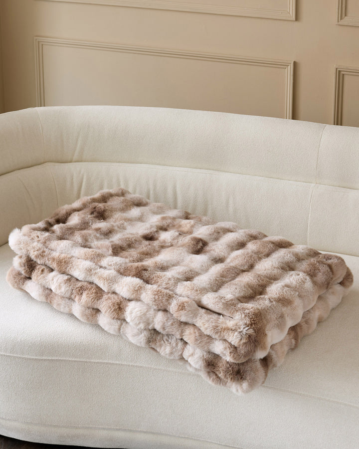 Nova throw blanket in natural, quilted pattern, draped on cream curved sofa.