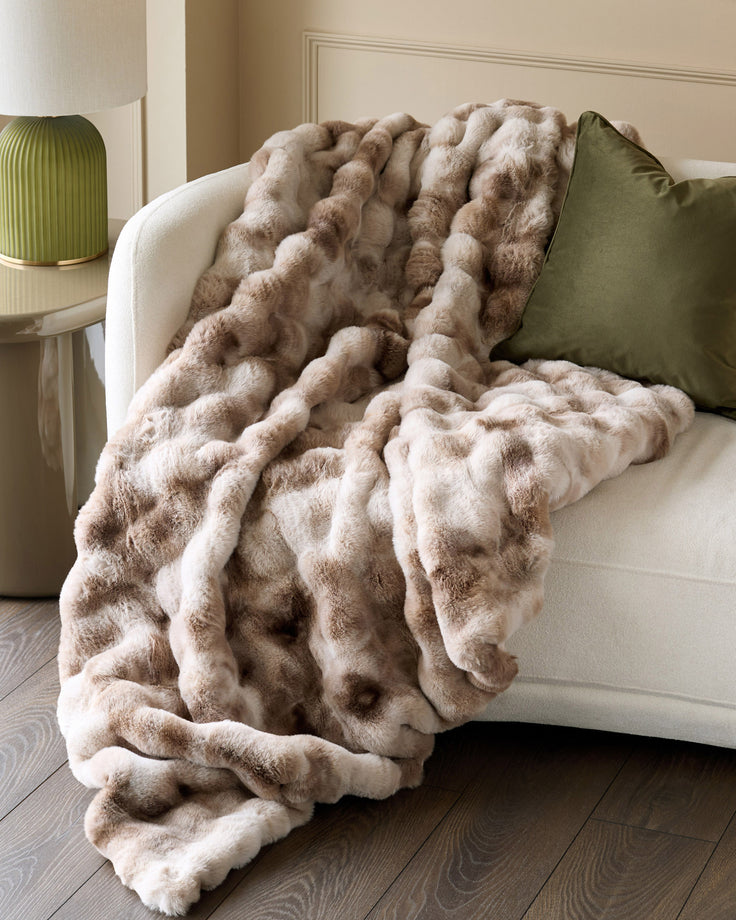Nova throw blanket in natural color draped over cream armchair with green pillow.
