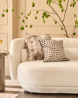 Nova cushion in natural, large size, displayed on a cream armchair in a styled living room setting.