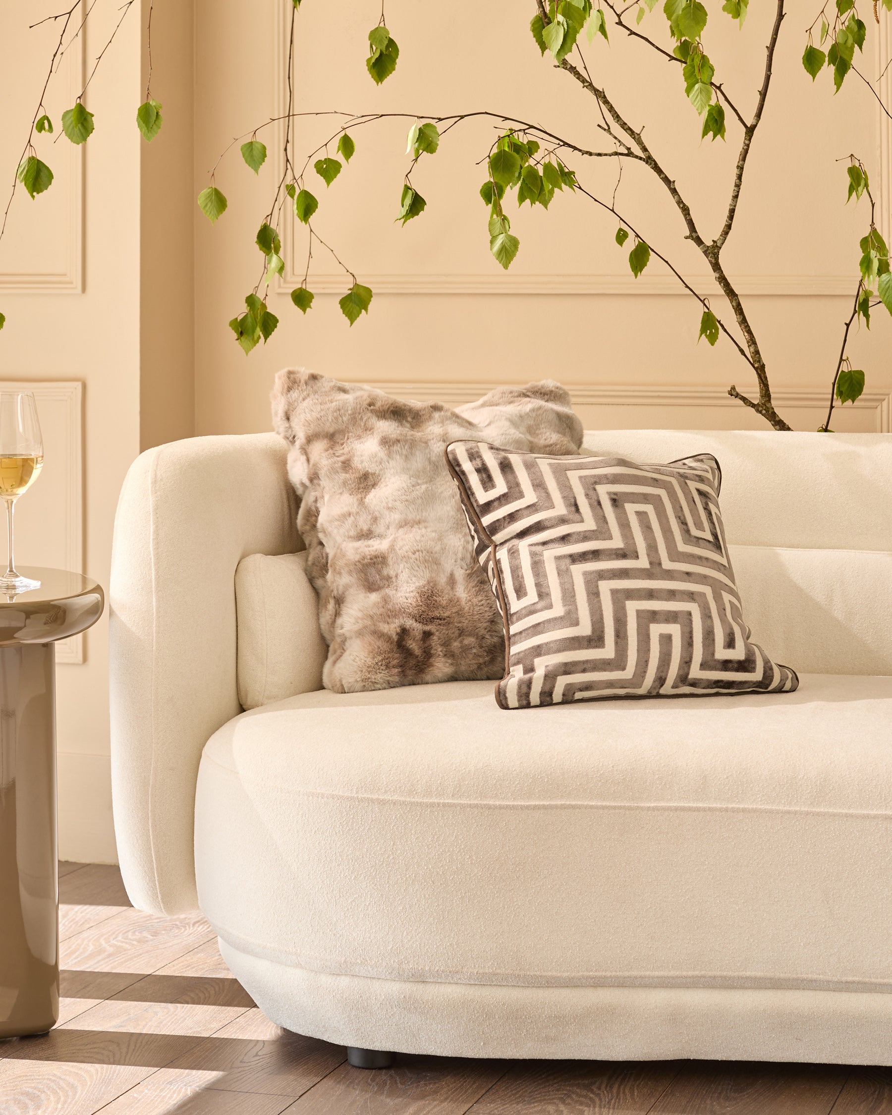 Nova cushion in natural, large size, displayed on a cream armchair in a styled living room setting.