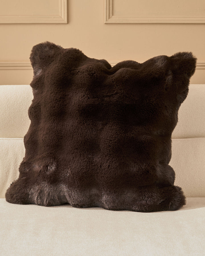 Nova cushion in chocolate brown faux fur with decorative ear-shaped corners, displayed on a cream sofa.