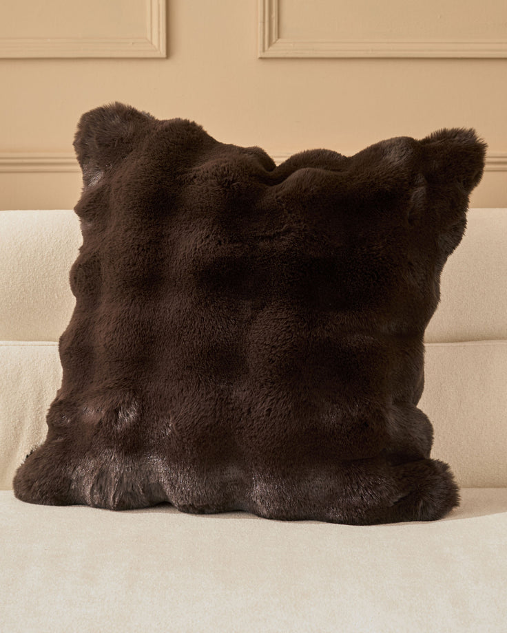 Nova cushion in chocolate brown faux fur with decorative ear-shaped corners, displayed on a cream sofa.