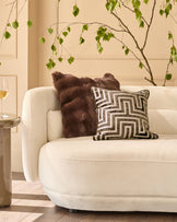 Chocolate brown faux fur cushion displayed on a cream armchair with geometric patterned pillow nearby.