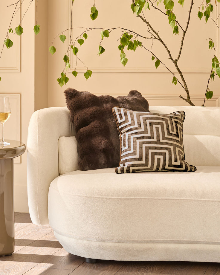 Large chocolate brown cushion displayed on a cream armchair with geometric patterned pillow.