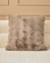 Large taupe plush cushion with quilted diamond pattern, displayed on a cream upholstered sofa against a beige paneled wall.
