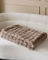 Nova throw in taupe, quilted texture, draped over a curved cream upholstered sofa.