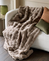 Nova throw in large taupe draped over a cream armchair, showcasing its plush texture and ruched design.