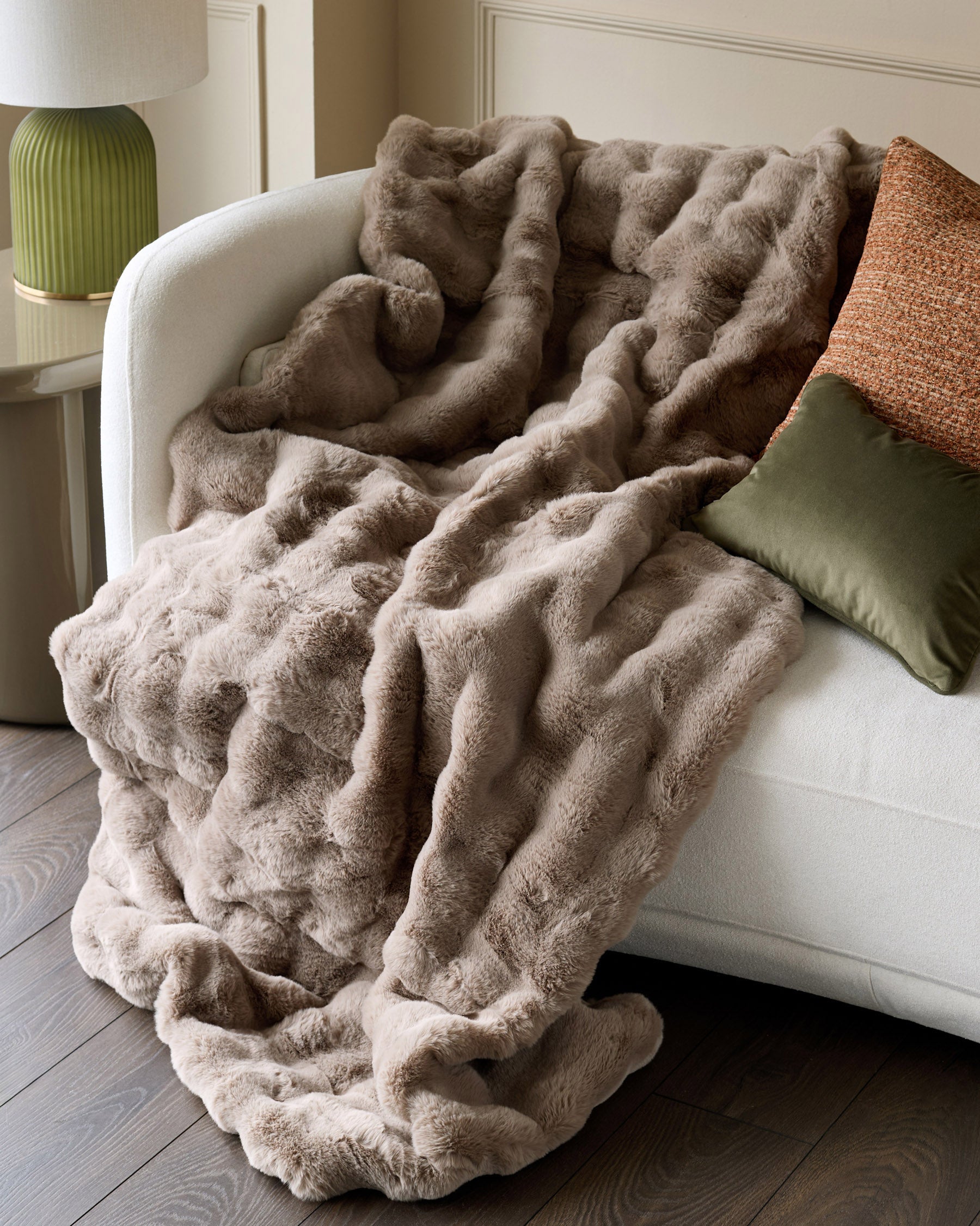 Nova throw in large taupe draped over a cream armchair, showcasing its plush texture and ruched design.