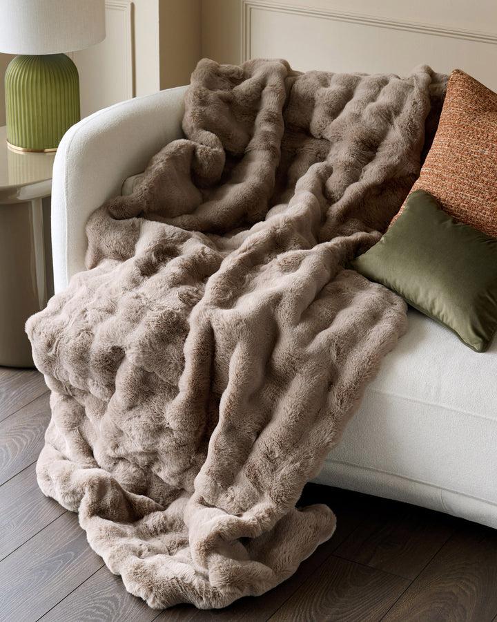 Nova throw in large taupe draped over a cream armchair, showcasing its plush texture and ruched design.