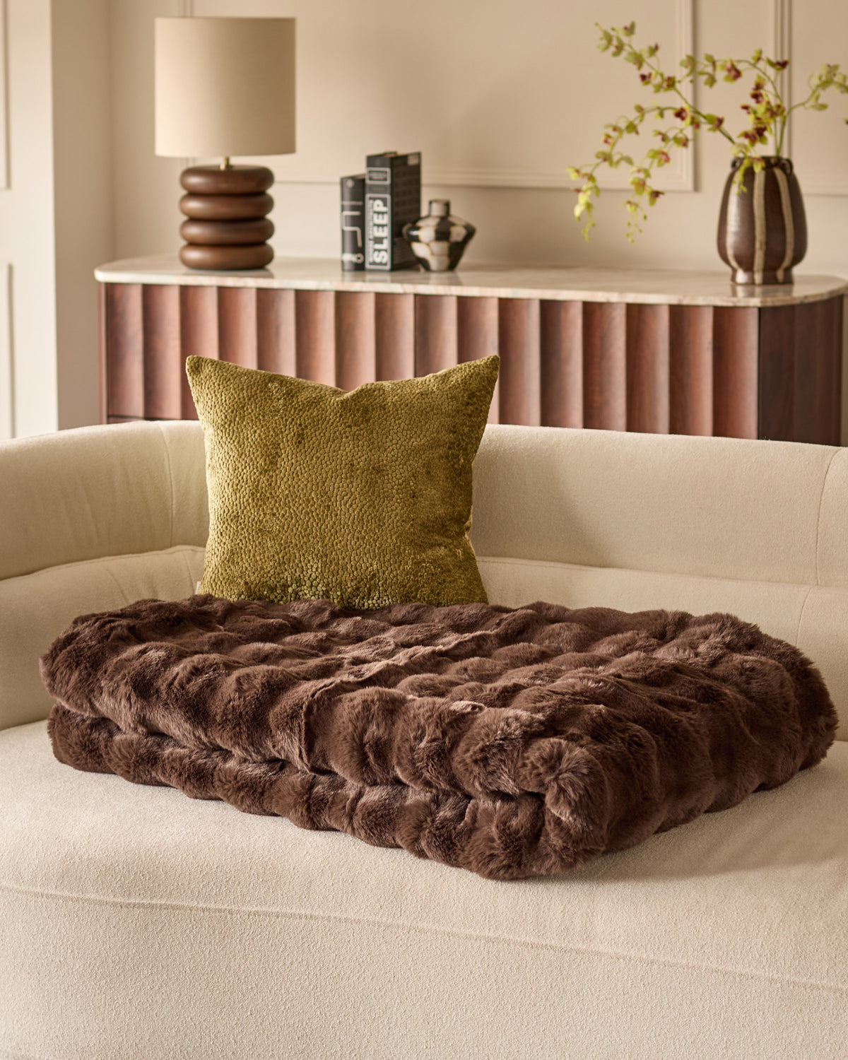 Harlene cushion in olive green displayed on a cream sofa with brown faux fur throw blanket, styled in modern living room setting.