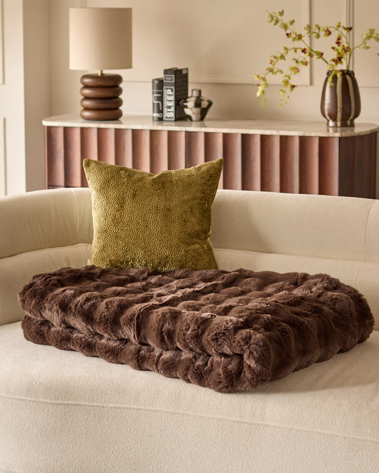 Harlene cushion in olive green displayed on a cream sofa with brown faux fur throw blanket, styled in modern living room setting.