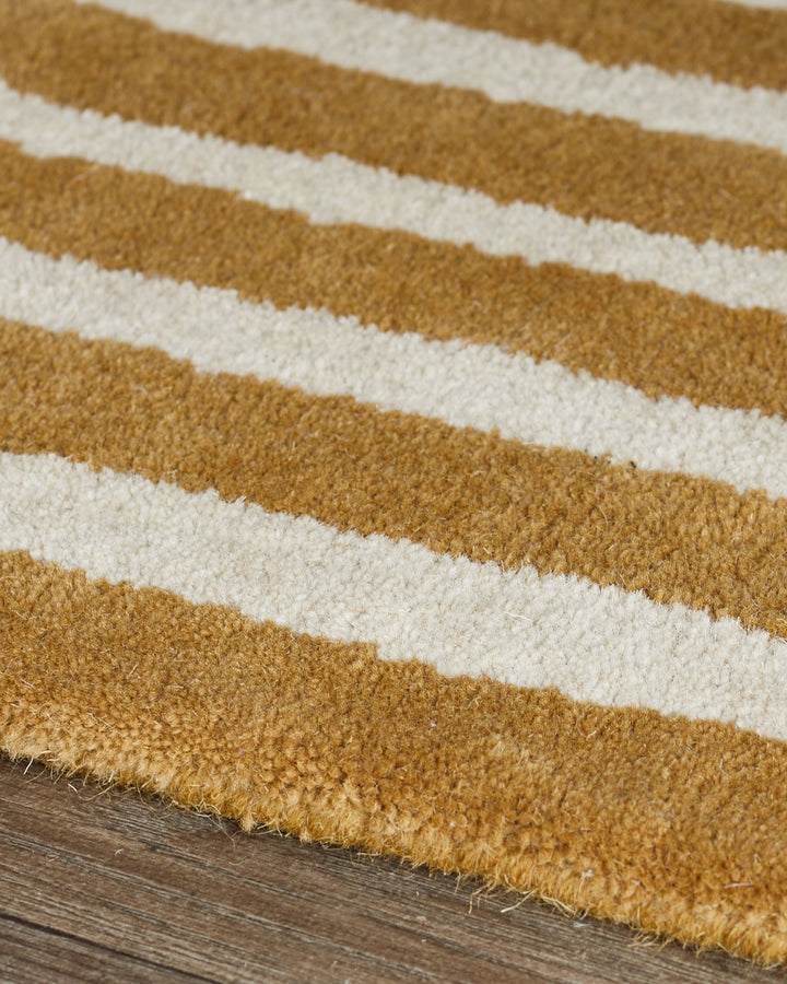Striped wool rug in ochre and cream with sculptural texture, displayed on wooden flooring.