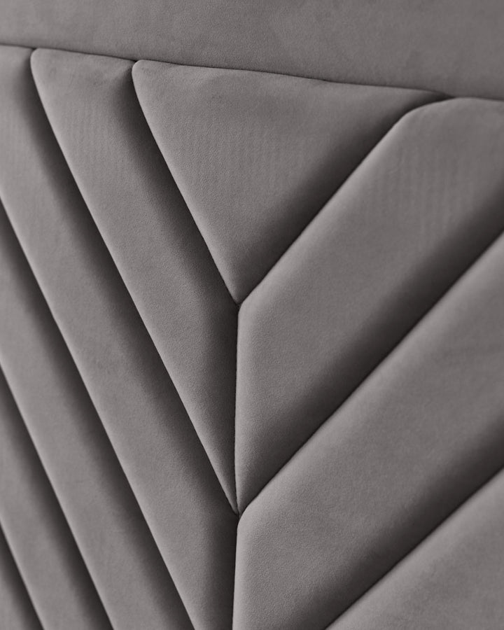 Close-up of a grey, padded headboard with a geometric, diamond-patterned design. Soft, luxurious and stylish bedroom furniture.