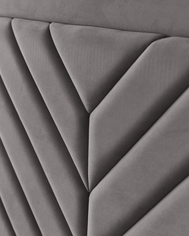 Close-up of a grey, padded headboard with a geometric, diamond-patterned design. Soft, luxurious and stylish bedroom furniture.