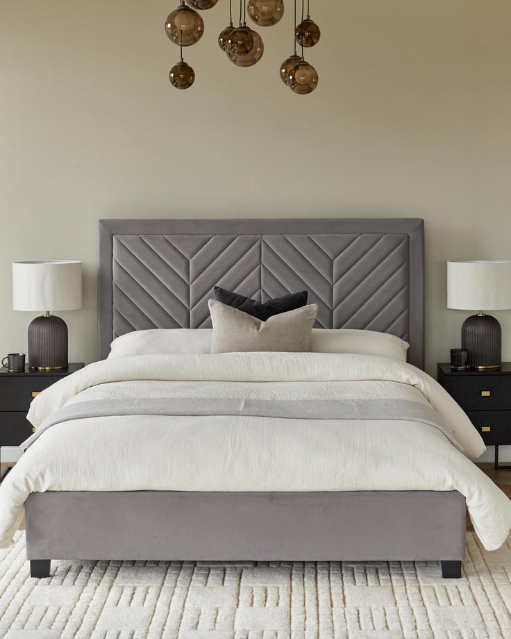 A stylish bedroom set featuring a grey upholstered bed frame, headboard, bedside tables, and table lamps.