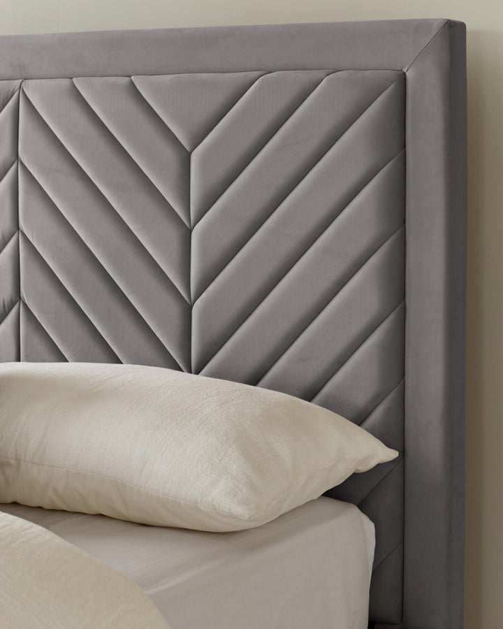A stylish grey velvet headboard with a geometric pattern, paired with a crisp white pillow and bedding.