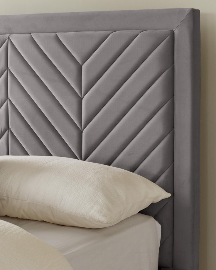 A stylish grey velvet headboard with a geometric pattern, paired with a crisp white pillow and bedding.