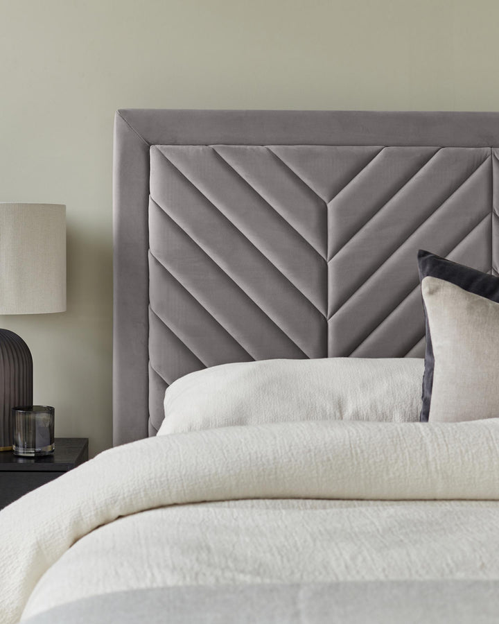 A stylish grey chevron headboard, with a cosy bed and bedside table, perfect for a modern bedroom.