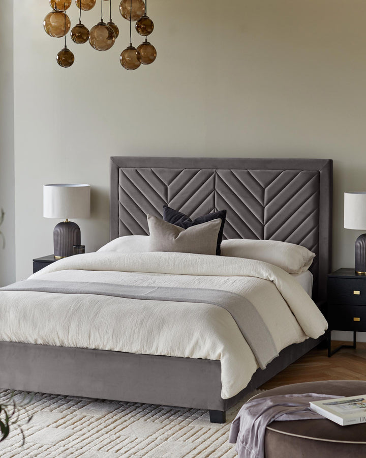 A stylish grey upholstered bed with chevron headboard. Lamps on bedside tables. Statement chandelier. A cosy, inviting bedroom.