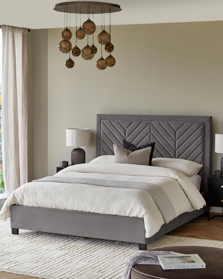 Bedroom with grey velvet bed, globe chandelier, bedside tables, cream rug and ottoman.