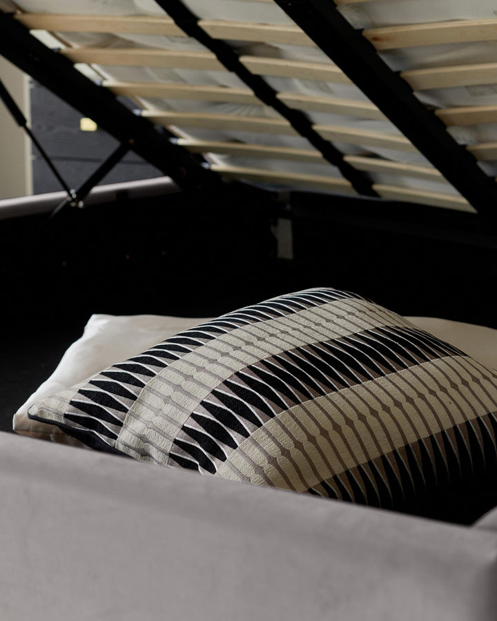 Stylish bed with integrated storage under the mattress and striped decorative cushion.