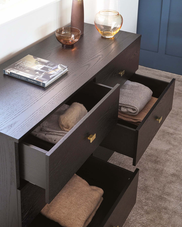 A sleek black wood console with open drawers holding neatly folded blankets, accented by decorative vases and a book on top.