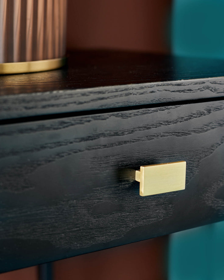 Close-up of a sleek, black wood drawer with a gold handle, showcasing modern furniture design.