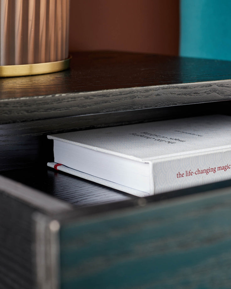 A wooden shelf unit with a book titled 'the life-changing magic' partially visible within a drawer.