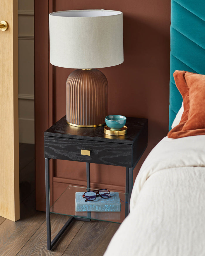 Bedside table with lamp, drawer and shelf. A book and glasses sit on the shelf.