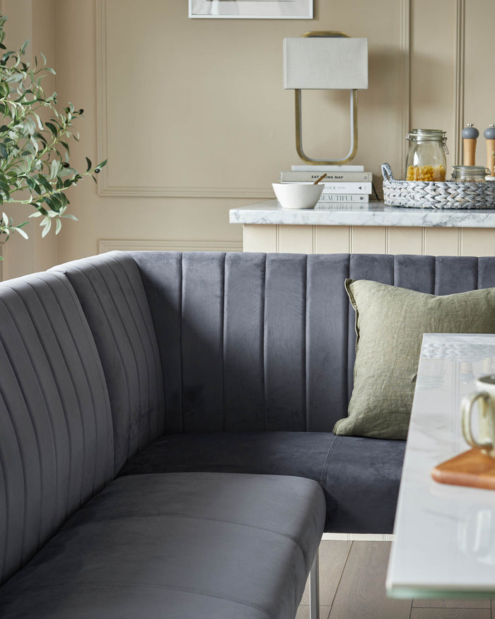 Stylish grey velvet corner dining bench with a green cushion, complemented by a marble-topped table. Modern kitchen design.