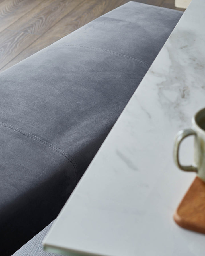 Close-up of a modern grey sofa and white marble table with a mug and wooden coaster. Contemporary design.