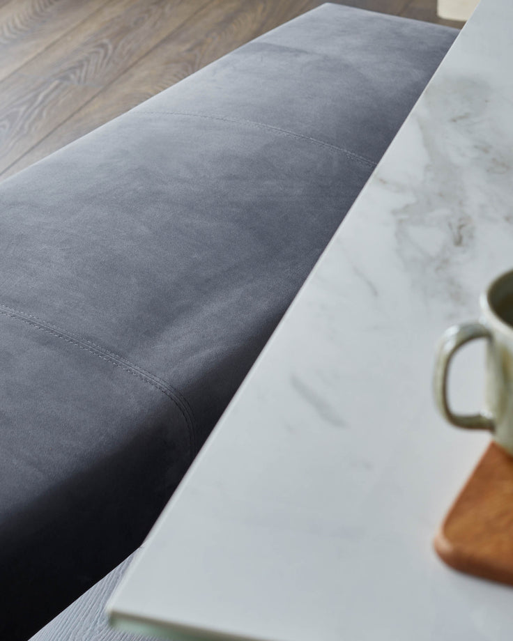 Close-up of a modern grey sofa and white marble table with a mug and wooden coaster. Contemporary design.