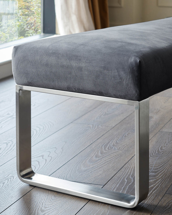 A grey velvet bench with polished metal legs, creating a modern and elegant furniture piece.