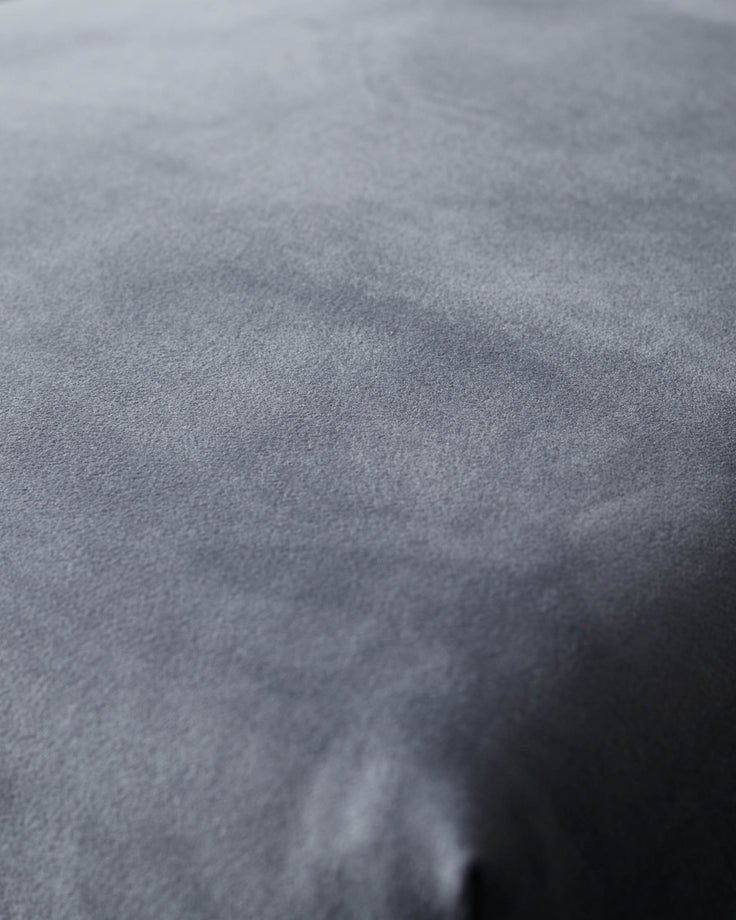 Close-up of a grey velvet cushion or sofa, showing the texture and subtle sheen of the fabric.