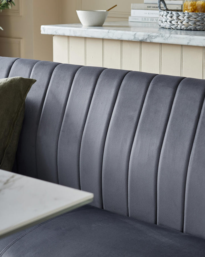 A grey upholstered banquette seating with a marble table top, books and a basket visible in the background.