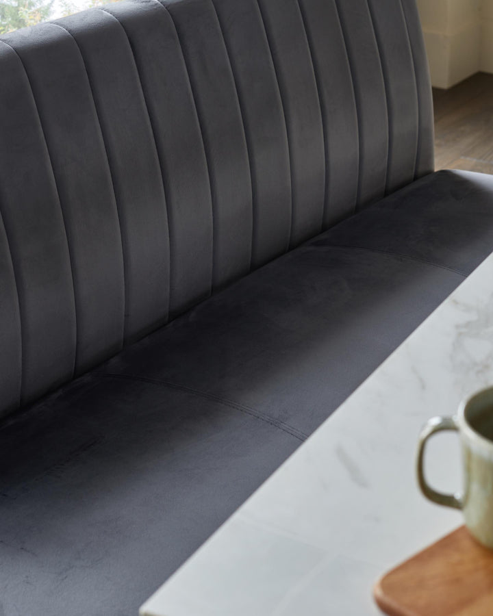 A stylish grey upholstered banquette seat and a white marble table with a cup on a wooden board.