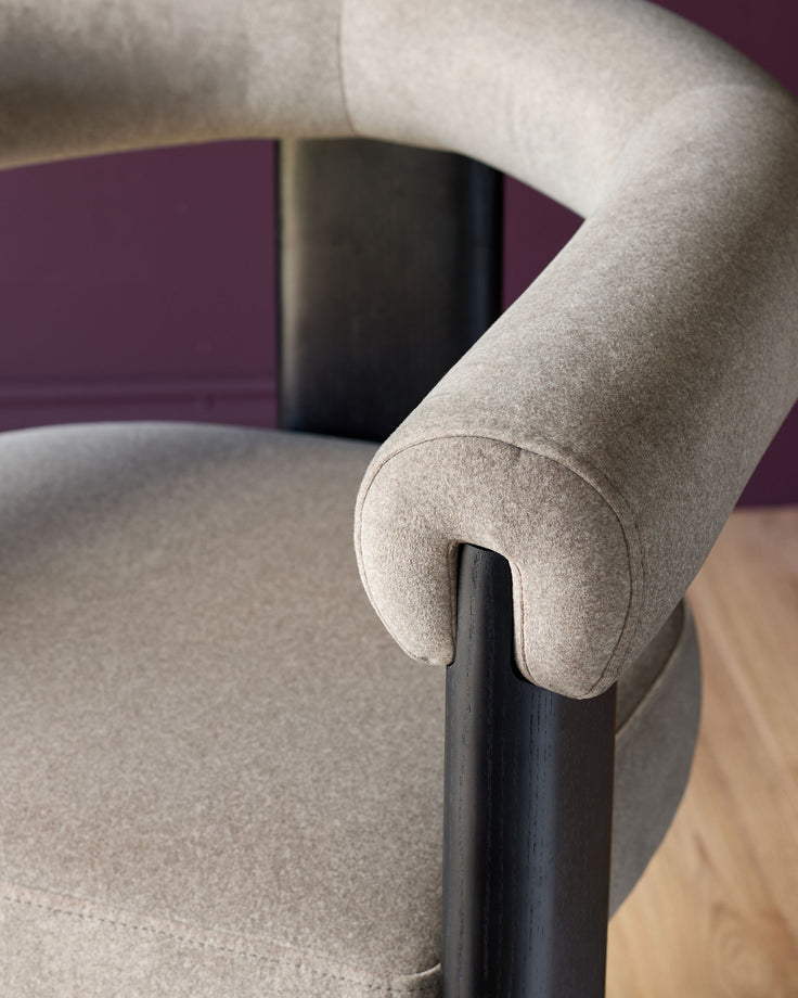Close-up of a stylish chair with curved armrest, showing the textured fabric and dark wood frame. Modern design for comfortable seating.
