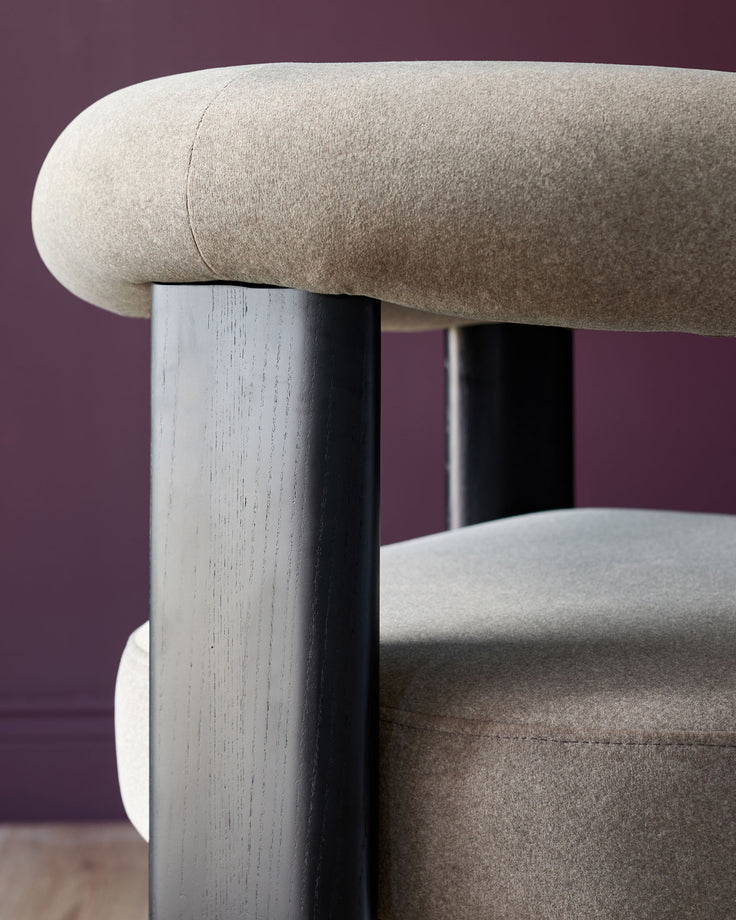 Close-up of a modern armchair with a rounded backrest and dark wood legs. Minimalist design with neutral upholstery.