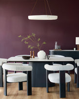 A modern dining set featuring upholstered chairs, a marble-look table, and a sideboard, all under a circular pendant light.